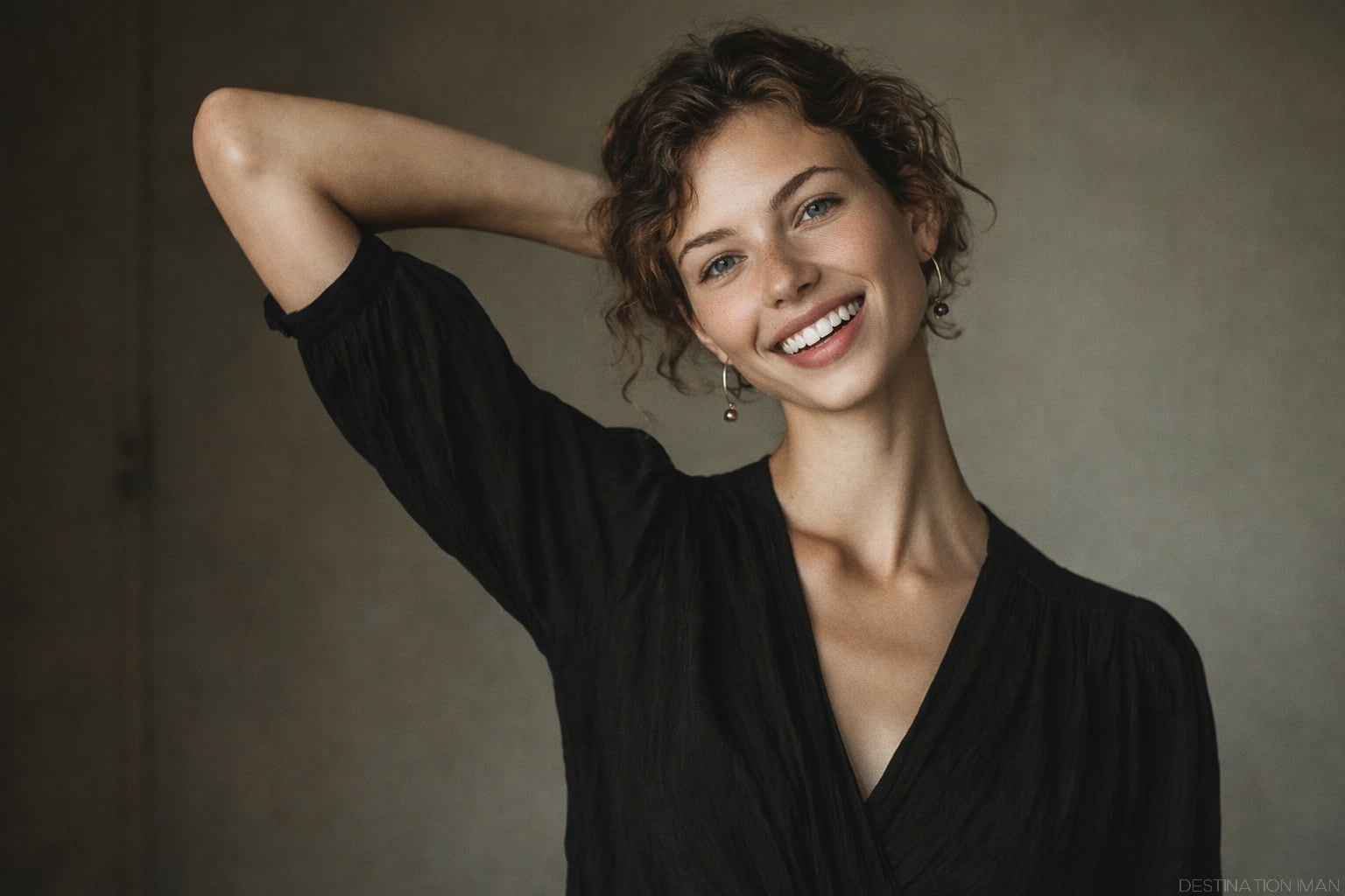 Editorial portrait with one arm raised behind the head, relaxed shoulders, elongated neck line, and a natural open smile