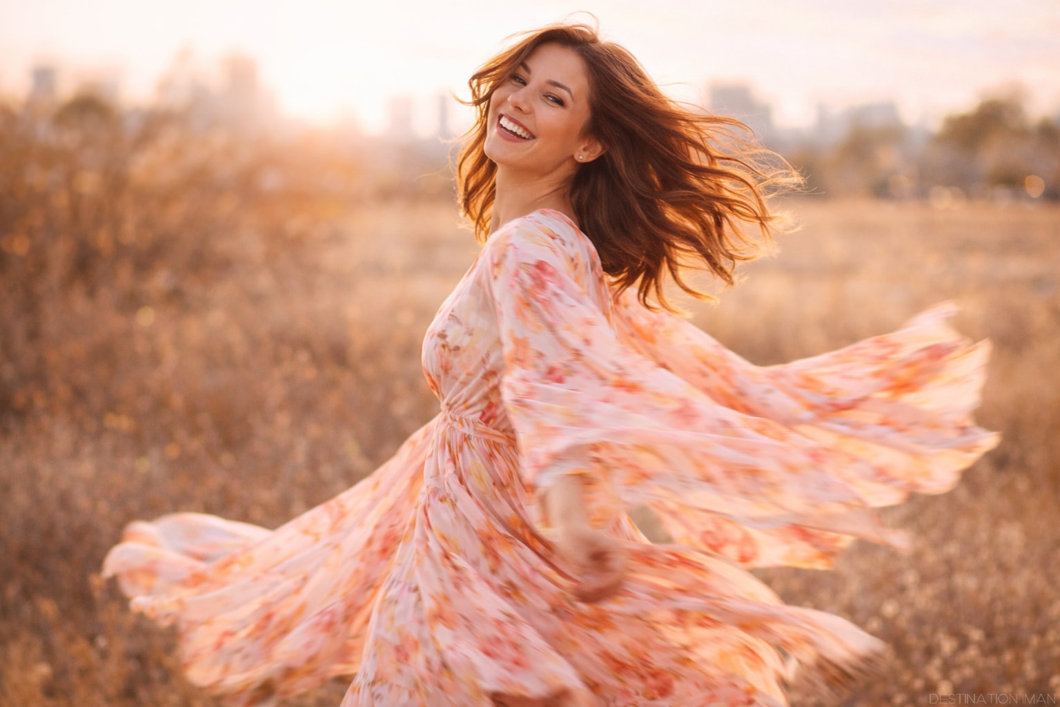 Woman spinning in flowing floral dress at golden hour, demonstrating dynamic posing with natural movement and genuine smile